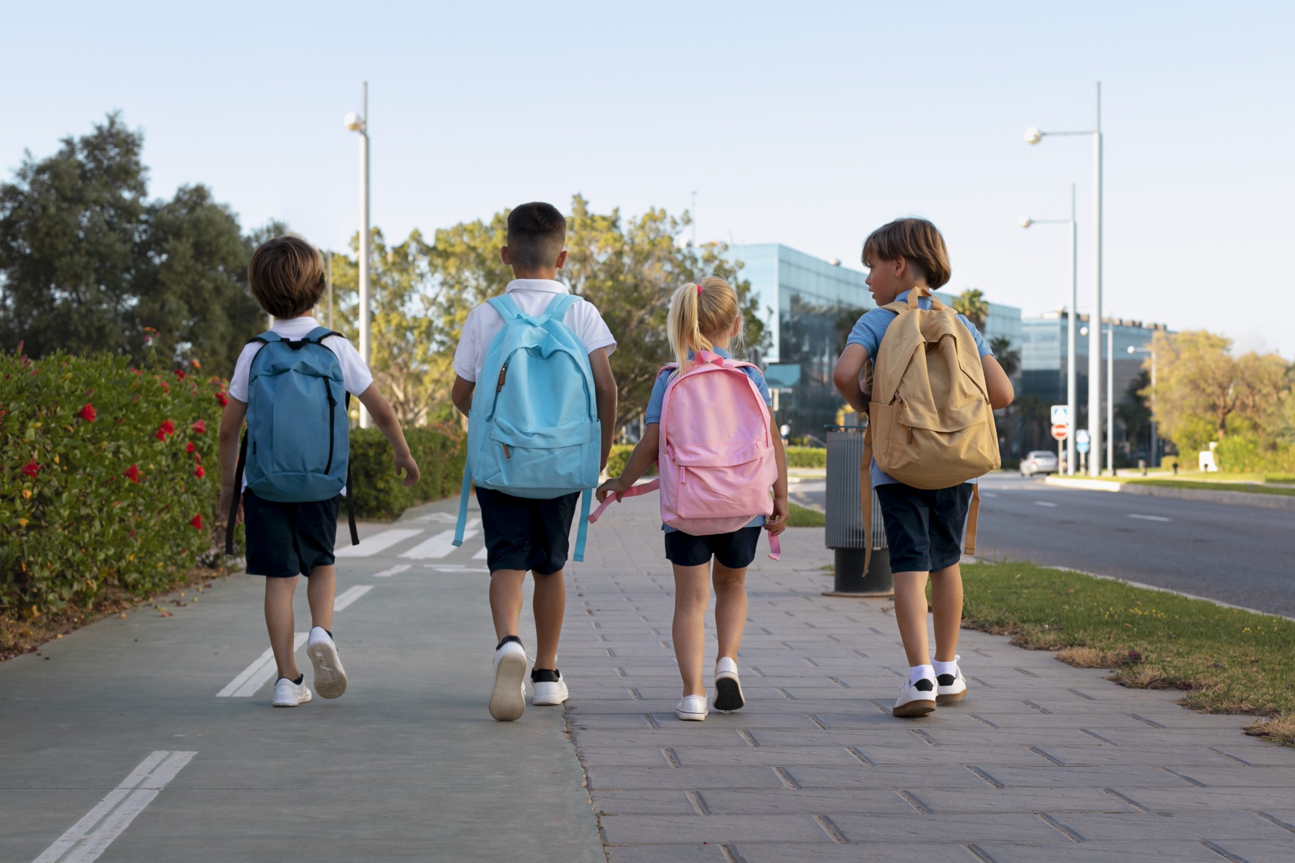 Four kids walk towards school, wearing their backpacks.
